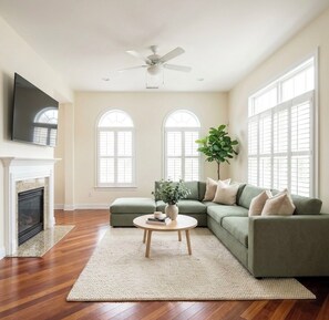 A living room with a sectional sofa, a fireplace, a flat-screen TV, and a ceiling fan. - Snowbird Desert Condo - Tennis Garden, Golf, 2BR/2BA (La Quinta)