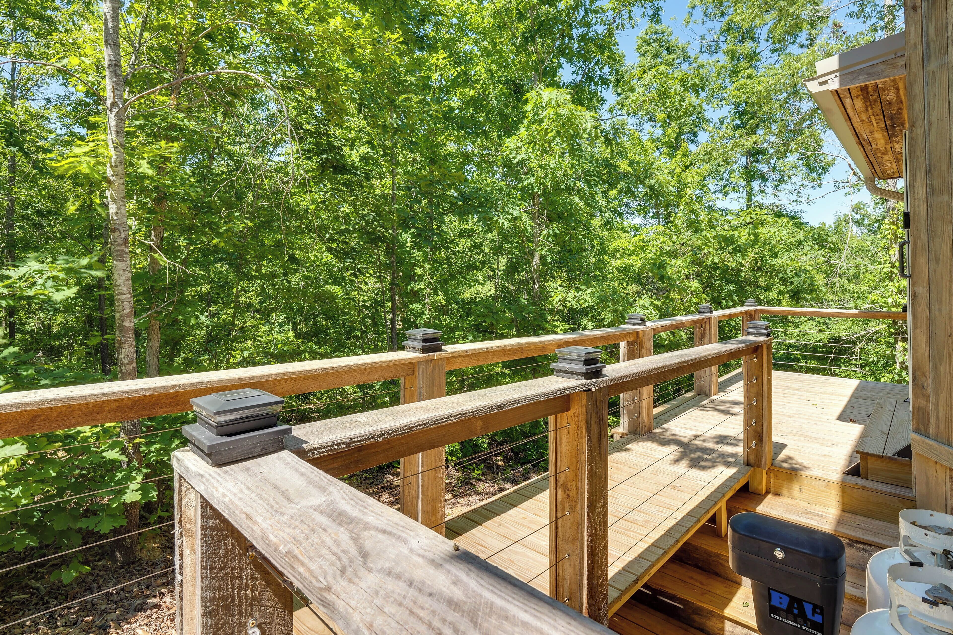 Una terraza de madera con baranda, rodeada de árboles.