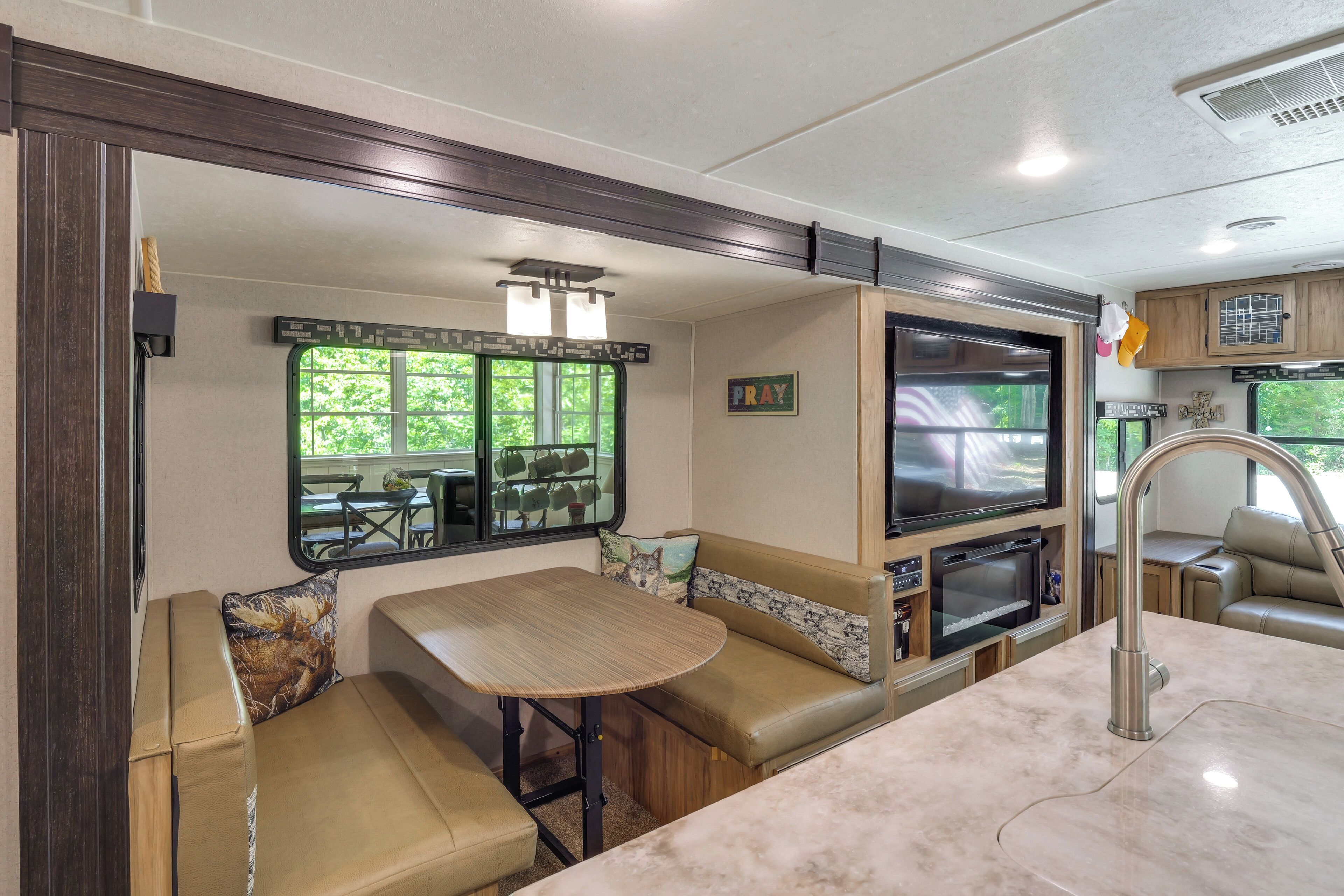 A compact RV kitchen with a dining area, a built-in TV, and a window offering a view of the outdoors.