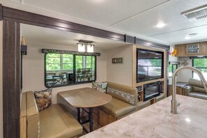 Cocina compacta para vehículos recreativos con comedor, televisor integrado y ventana con vistas al exterior.