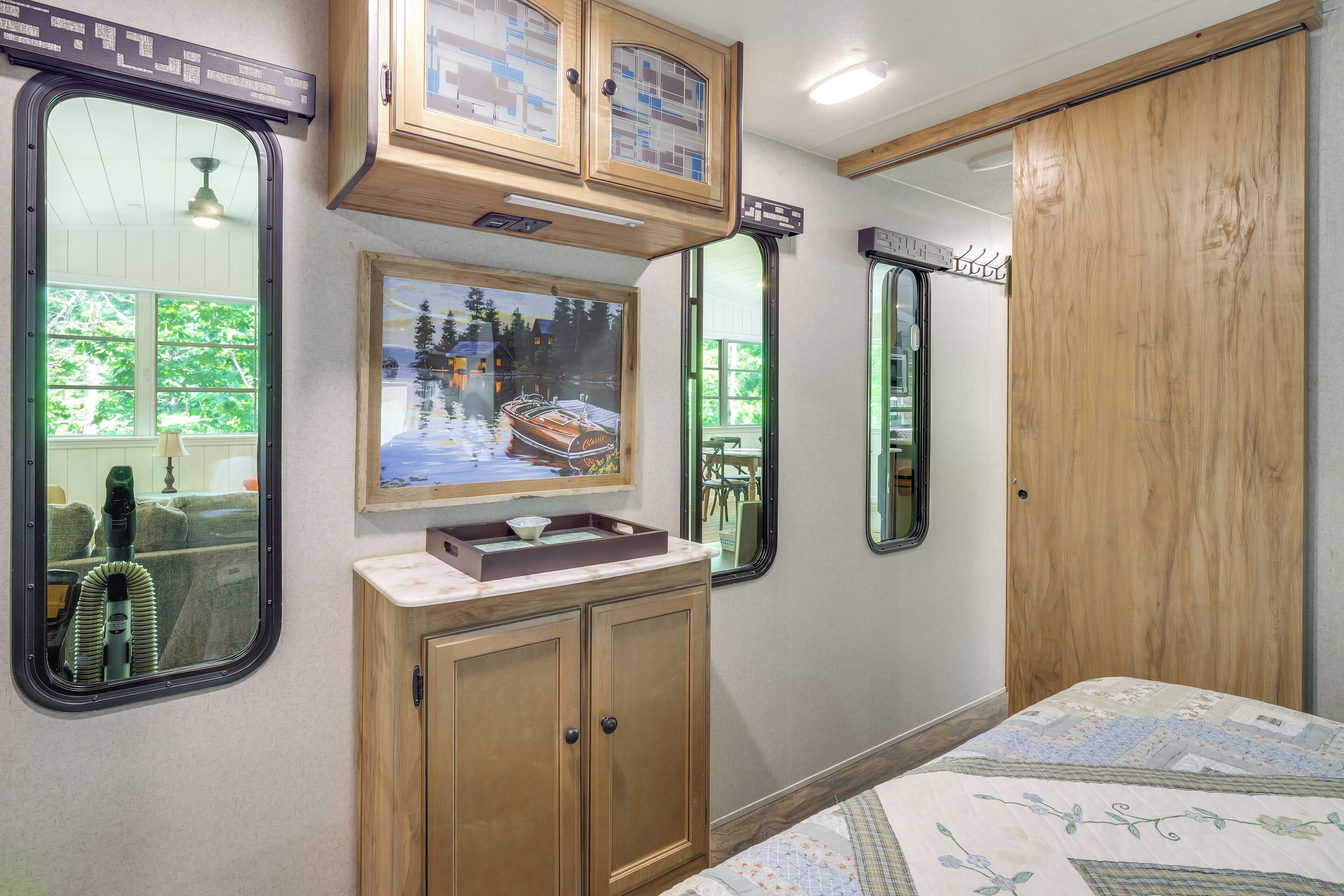 A bedroom with a wooden cabinet, a painting, a mirror, and a bed with a floral bedspread.