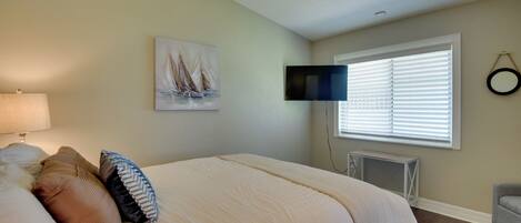 A bedroom with a bed, a TV mounted on the wall, a window with blinds, and a painting on the wall.