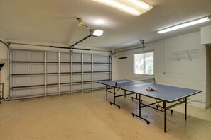 Um quarto com mesa de pingue-pongue, porta de garagem e janela com persianas.