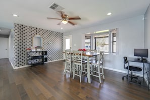 A spacious room with a dining table, chairs, a TV, and a ceiling fan.