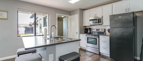 A modern kitchen with a central island, stainless steel appliances, and a view to the outside.