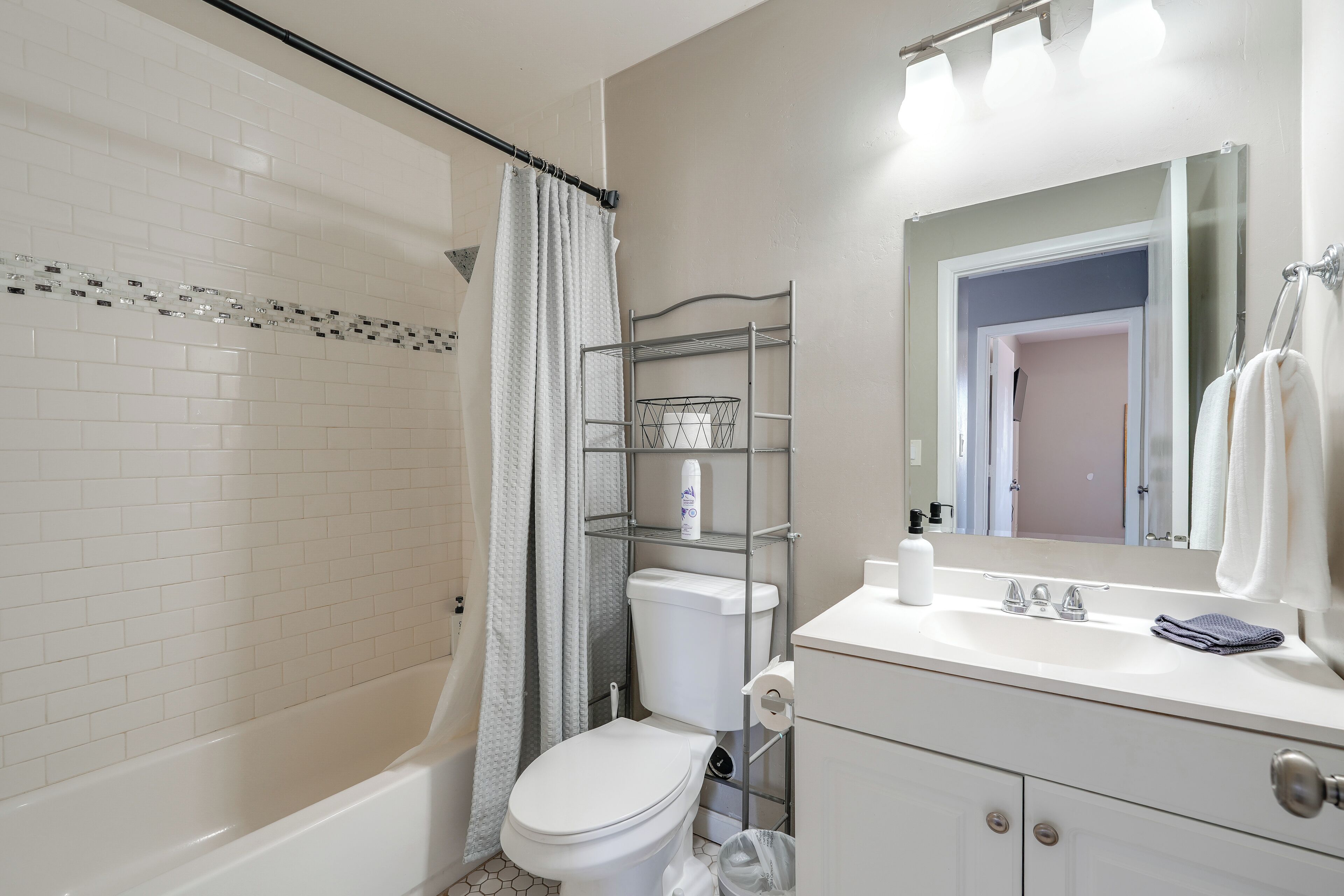 A bathroom with a white bathtub, toilet, and sink. There is a shower curtain, a mirror above the sink, and a towel rack.