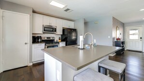 Una cocina moderna con armarios blancos, un refrigerador de acero inoxidable, un microondas y una isla grande con taburetes.
