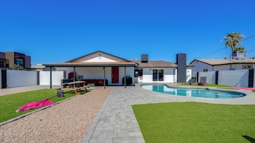 Un jardin à l’arrière d’une maison, avec une piscine, un patio couvert et une pelouse.