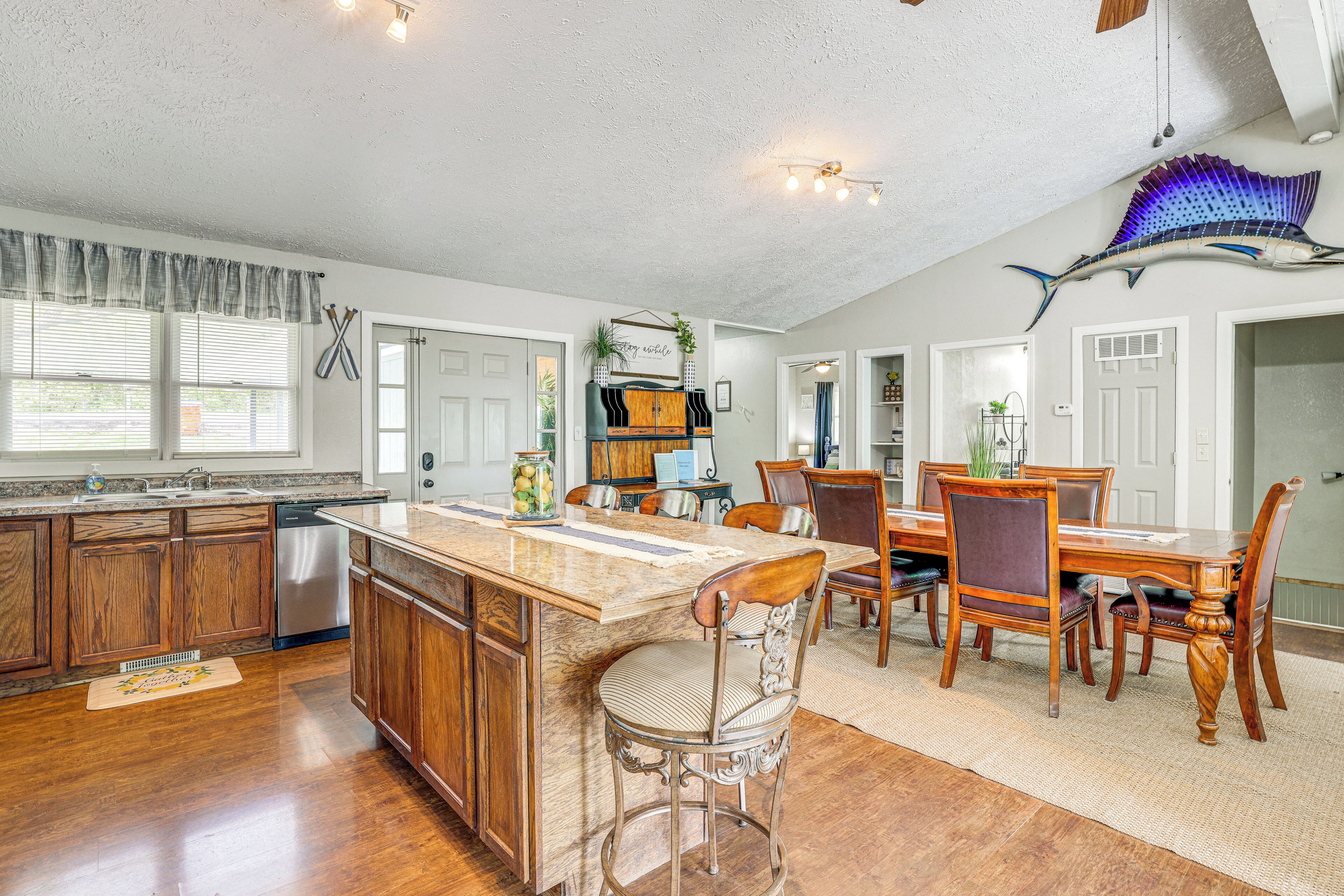 A spacious kitchen with wooden cabinets, a stainless steel dishwasher, and a large island with bar stools.