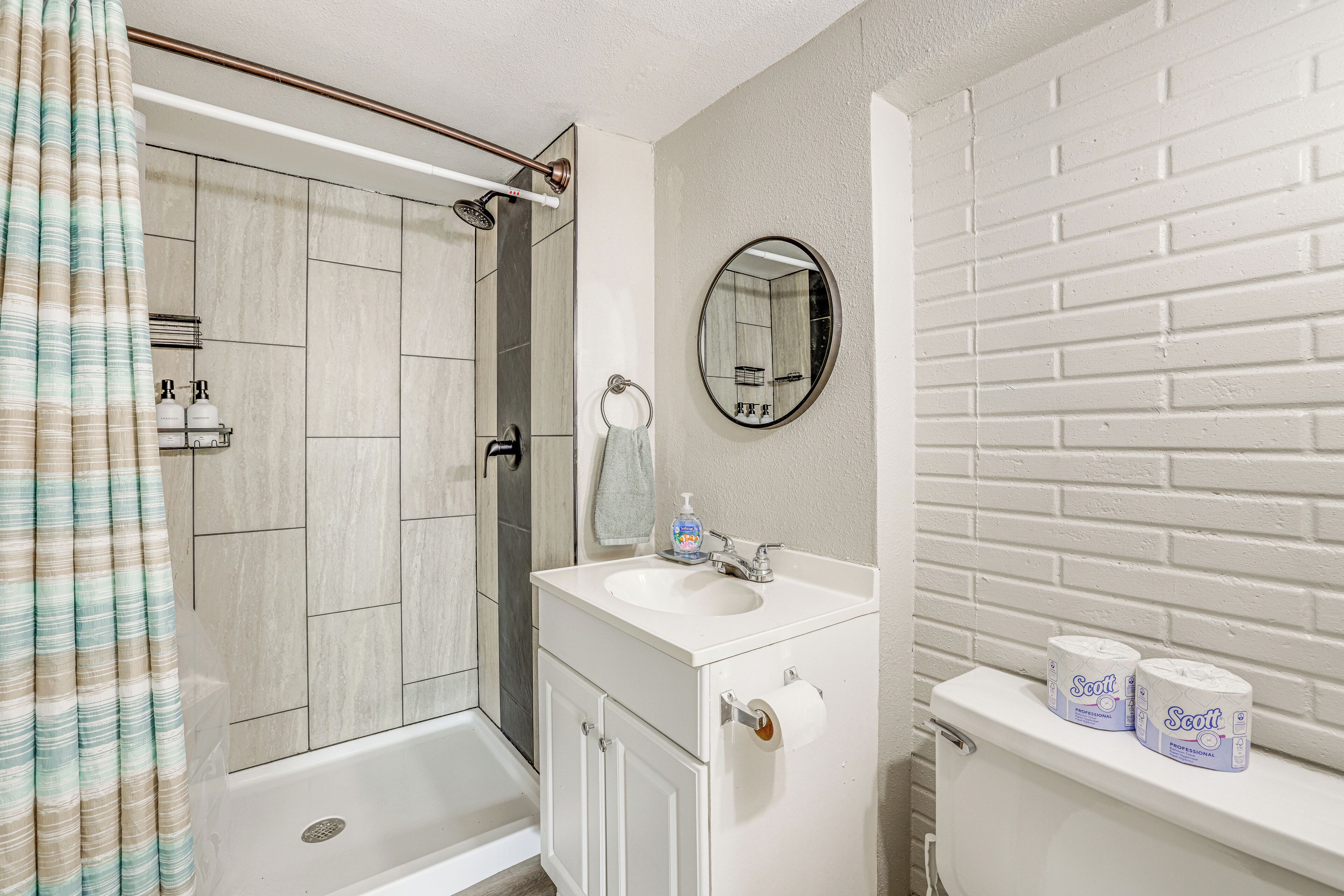 A bathroom with a shower, toilet, sink, and a mirror.