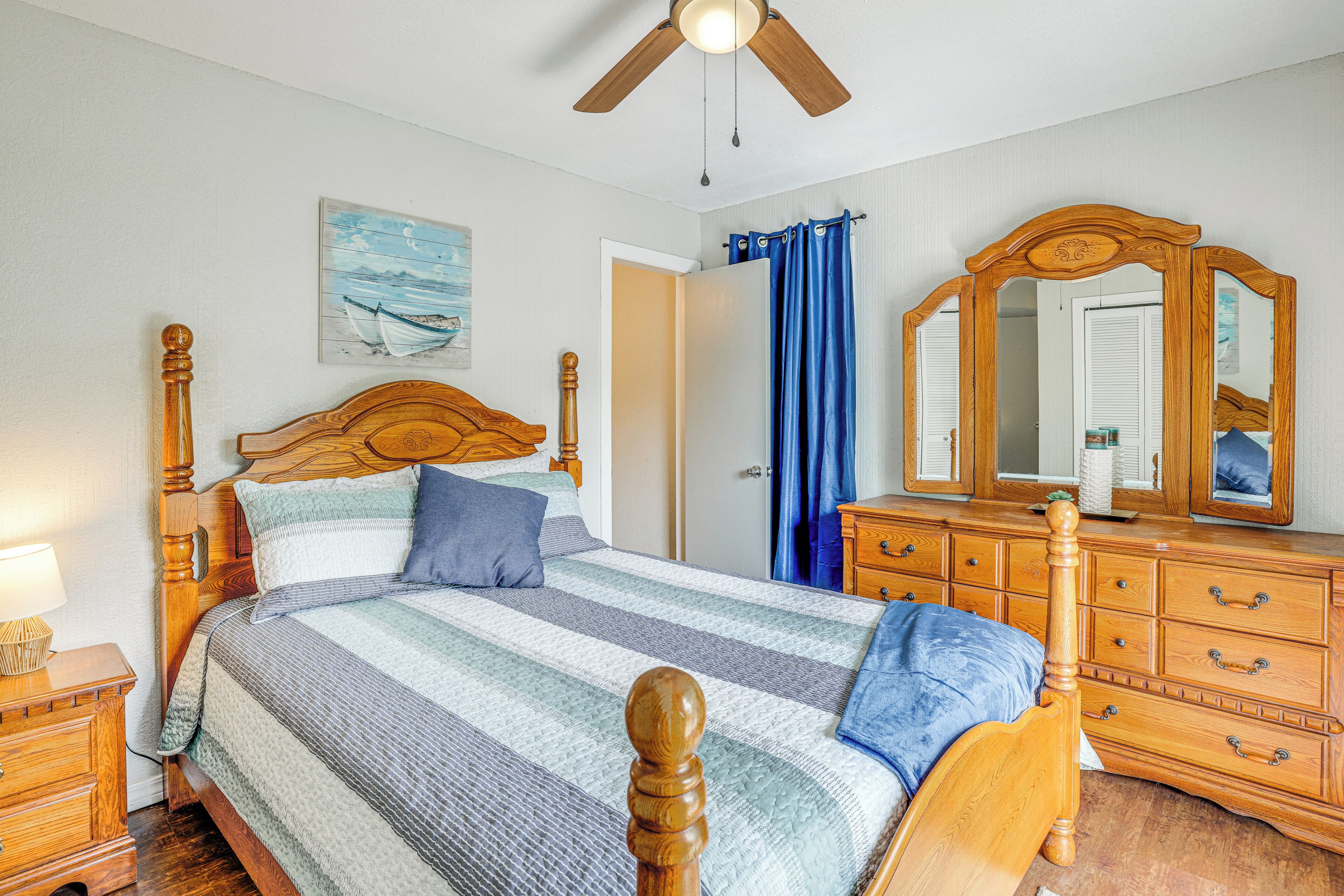 A bedroom with a wooden bed, a nightstand, a dresser, a ceiling fan, and a painting on the wall.