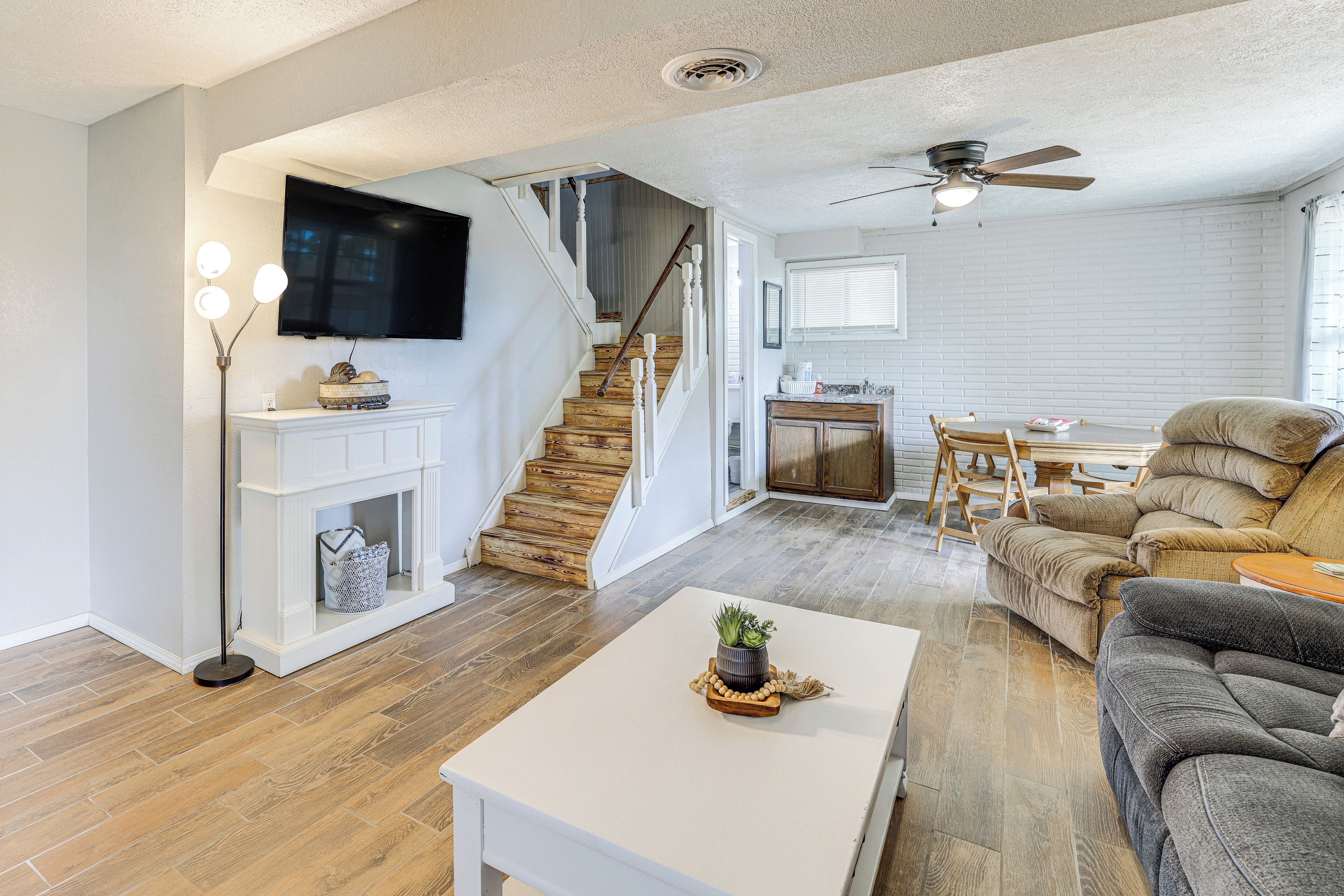 A spacious living area with a staircase, a flat-screen TV mounted above the fireplace, a ceiling fan, and a cozy seating arrangement.