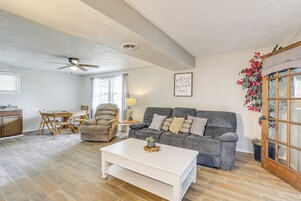 A living room with a grey sofa, white coffee table, wooden flooring, and a ceiling fan.