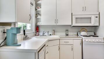 A kitchen with white cabinets, a microwave, a stove, and a coffee maker.