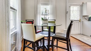 Un comedor con mesa de vidrio rodeada de sillas, una planta en maceta y vistas al exterior a través de una ventana con cortinas.