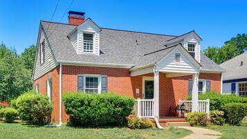 A two-story brick house with a front porch, a chimney, and a well-maintained lawn.