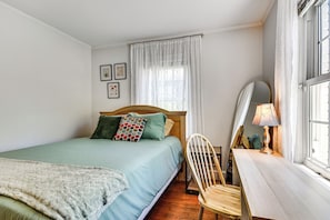Ein Schlafzimmer mit Bett, Sessel, Schreibtisch und einem Fenster mit Vorhängen.