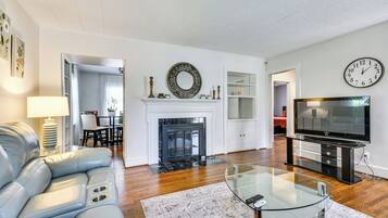 A modern living room with a leather sofa, a glass coffee table, a fireplace, a television, and a clock on the wall.