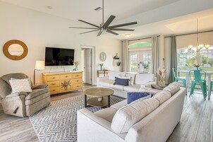 A modern living room with a ceiling fan, a flat-screen TV, a wooden cabinet, a sofa, a coffee table, and a dining area with chairs.
