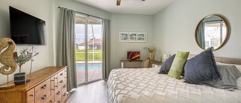A bedroom with a bed, dresser, television, and a view of a swimming pool through a glass door.