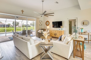 A spacious living room with a ceiling fan, a sofa set, a television, and a dining area with a table and chairs. - 8 Mi to Englewood Beach! Canal-front Family Haven (Rotonda West)