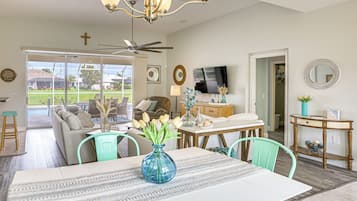 A spacious living area with a dining table, chairs, a sofa, and a television.