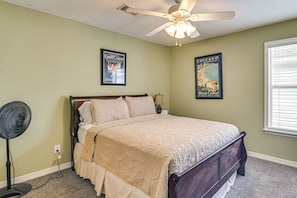 A bedroom with a bed, a ceiling fan, a standing fan, and two travel posters on the wall.