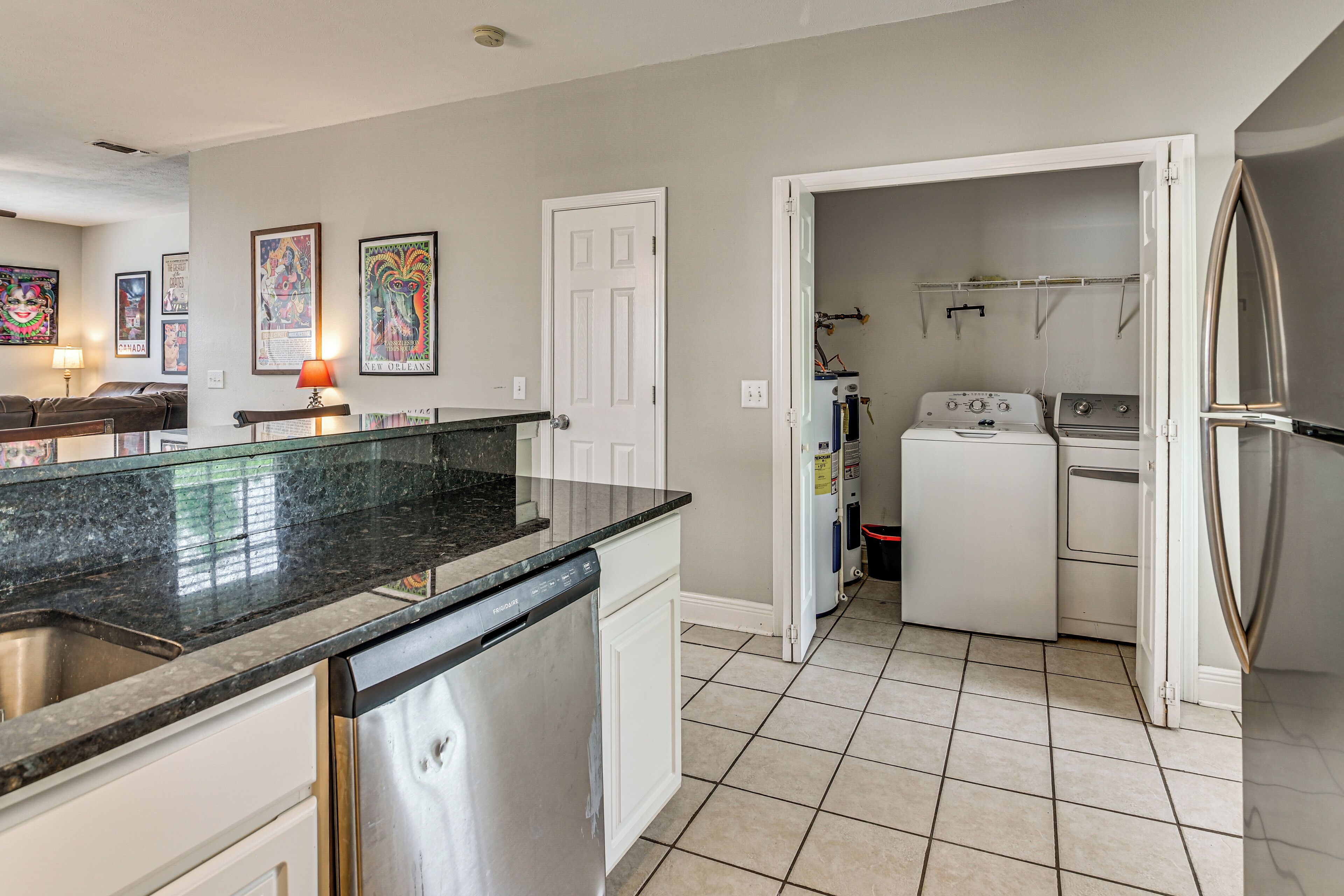 A kitchen with a granite countertop, white cabinetry, a dishwasher, a washing machine, and a refrigerator.