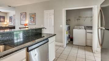 A kitchen with a granite countertop, white cabinetry, a dishwasher, a washing machine, and a refrigerator.