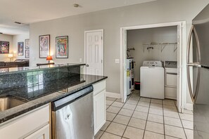 A kitchen with a granite countertop, white cabinetry, a dishwasher, a washing machine, and a refrigerator.