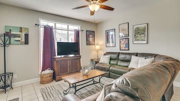 Un salon avec un canapé en cuir, une table basse, un téléviseur et un ventilateur de plafond.