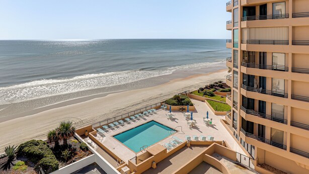 A beachfront hotel with a pool, lounge chairs, and a view of the ocean. - Dream Daytona Getaway: Beachfront Condo! (Daytona Beach Shores)