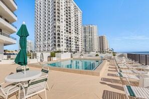 A pool area with lounge chairs and a table, surrounded by high-rise buildings. - Dream Daytona Getaway: Beachfront Condo! (Daytona Beach Shores)