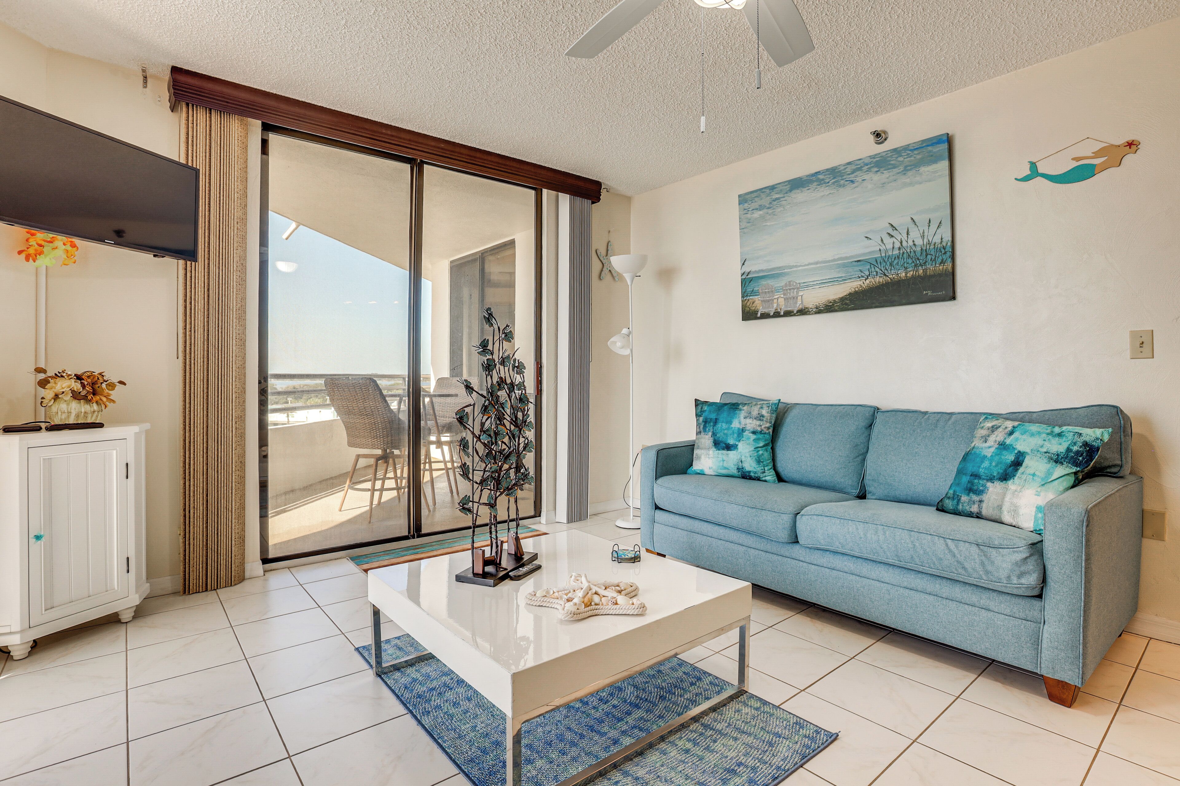 A living room with a sofa, a coffee table, a painting, and a view through a sliding door.