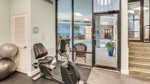 A fitness room with exercise equipment, a door leading to a pool area, and a staircase. - Dream Daytona Getaway: Beachfront Condo! (Daytona Beach Shores)