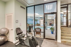 Ein Fitnessraum mit Trainingsgeräten, einer Tür zum Poolbereich und einer Treppe.
