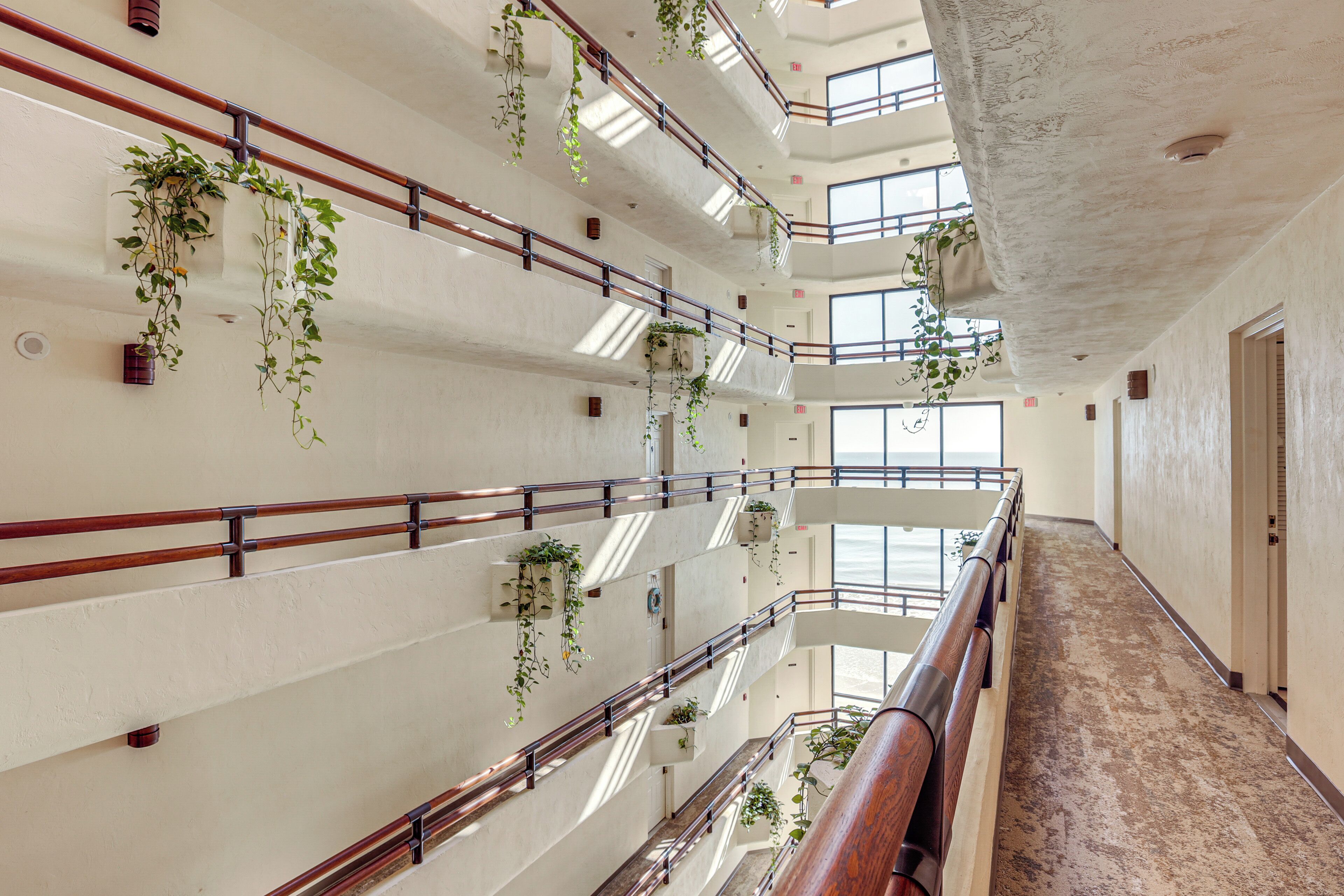 A multi-level interior with a central staircase, railings, and hanging plants.