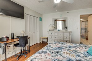 Ein Schlafzimmer mit Bett, Schreibtisch, Stuhl, Kommode und Deckenventilator.