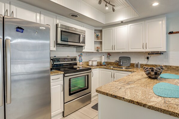 A modern kitchen with stainless steel appliances, white cabinetry, and granite countertops. - Dream Daytona Getaway: Beachfront Condo! (Daytona Beach Shores)