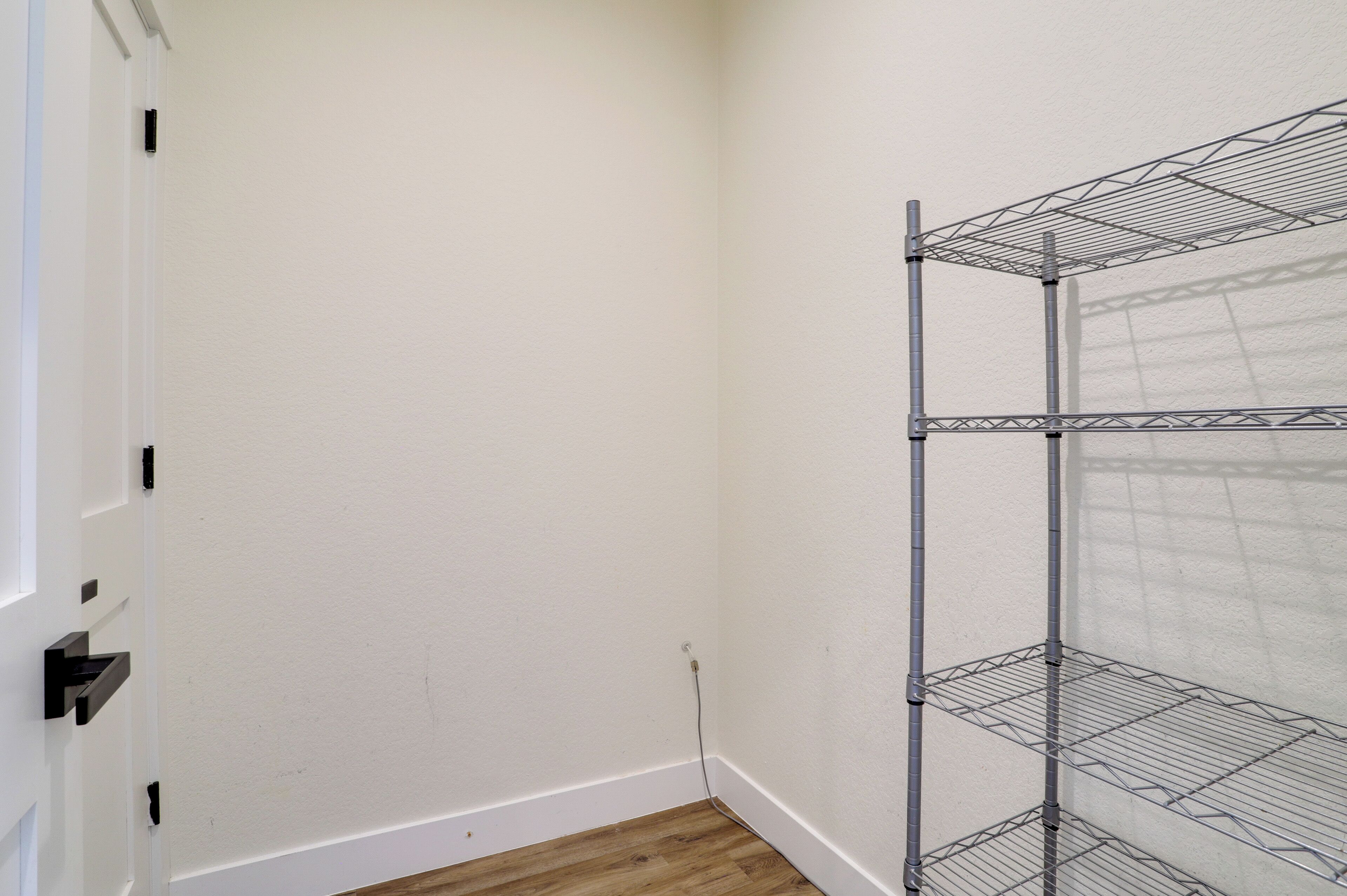 A corner of a room with a white wall, a wooden floor, and a metal shelving unit against the wall.