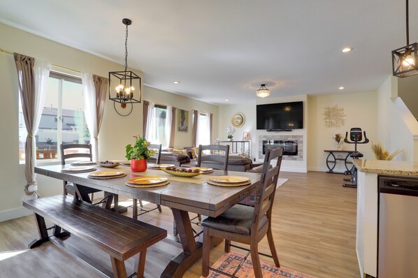 A dining area with a wooden table set for four, a sofa, and a television in the background. - Updated Family Home w/ Patio in Brighton (Brighton)