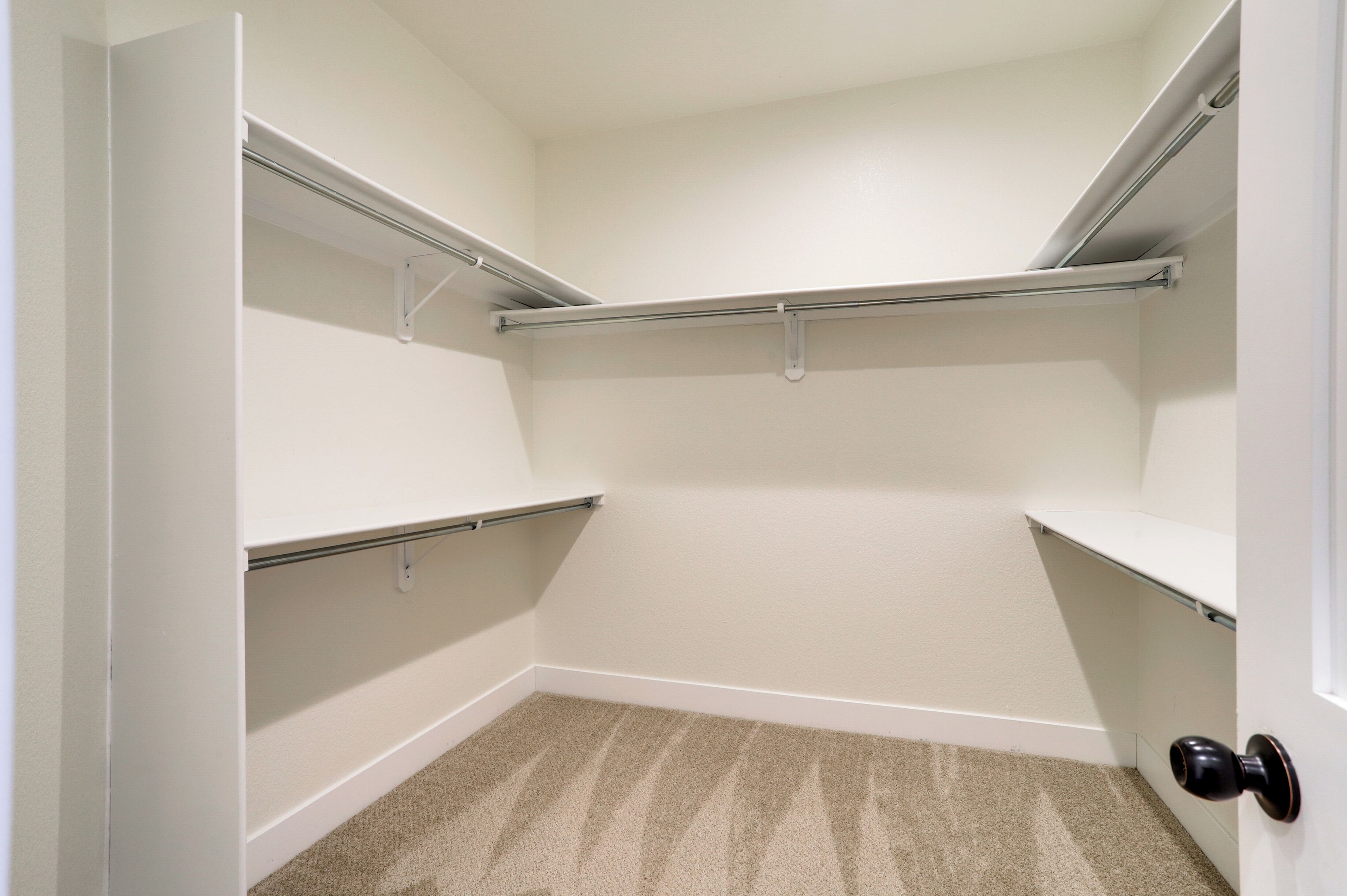 A walk-in closet with white walls, a carpeted floor, and metal shelving units.