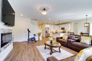 A modern living room with a fireplace, a sofa, a coffee table, and a kitchen in the background. - Updated Family Home w/ Patio in Brighton (Brighton)