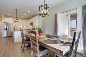 A modern kitchen with white cabinets, a stainless steel refrigerator, and a dining area with wooden chairs and a table set for four. - Updated Family Home w/ Patio in Brighton (Brighton)