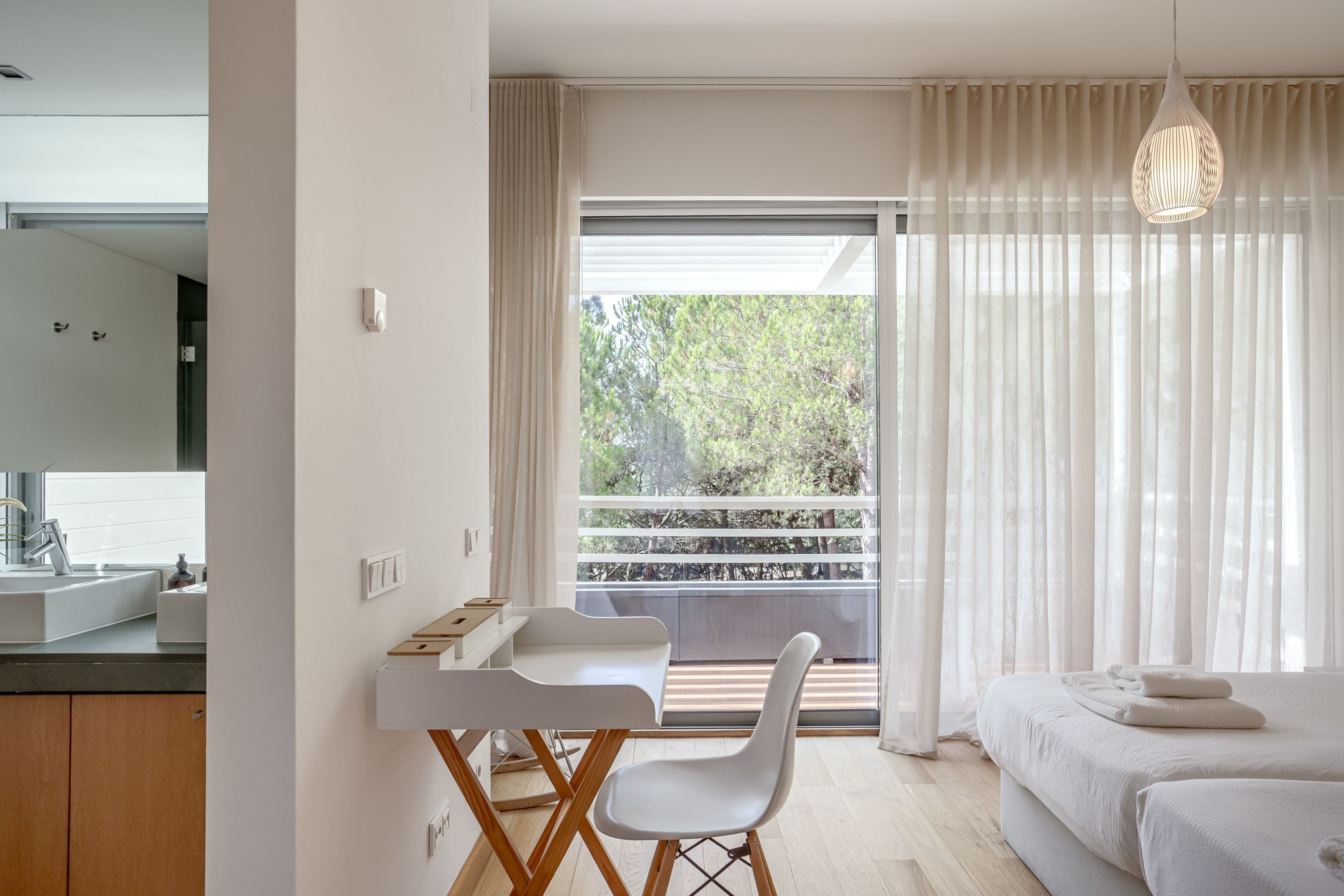 Un dormitorio moderno con balcón, escritorio y baño con lavamanos.