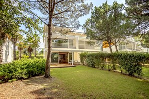 Uma casa moderna com varanda coberta, gramado e diversas árvores.