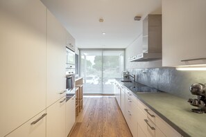 A modern kitchen with a central island, wooden flooring, and a view through the glass door. - Troia Atlantic Villa by Homing (Grandola)