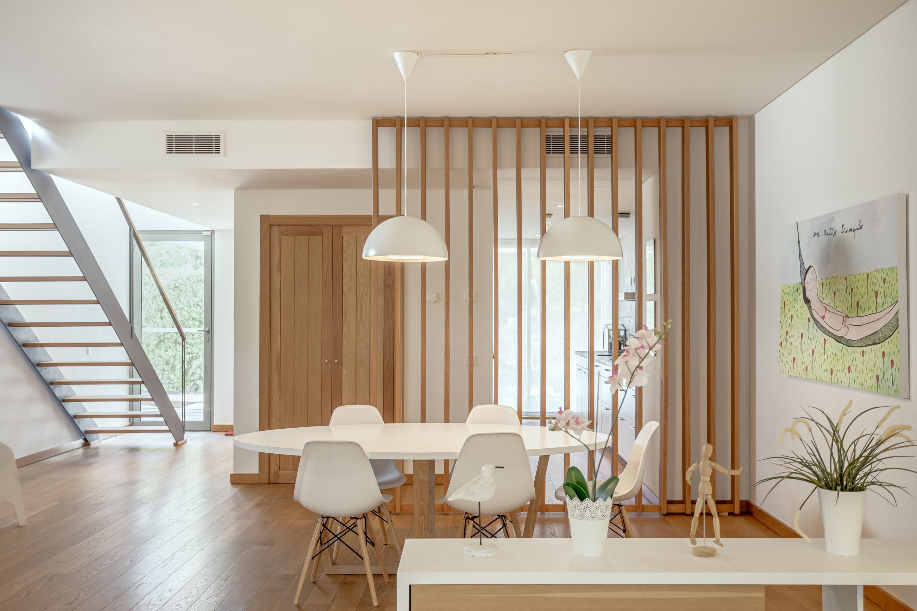 Un comedor moderno con una mesa blanca, sillas, lámparas colgantes y un separador de madera.