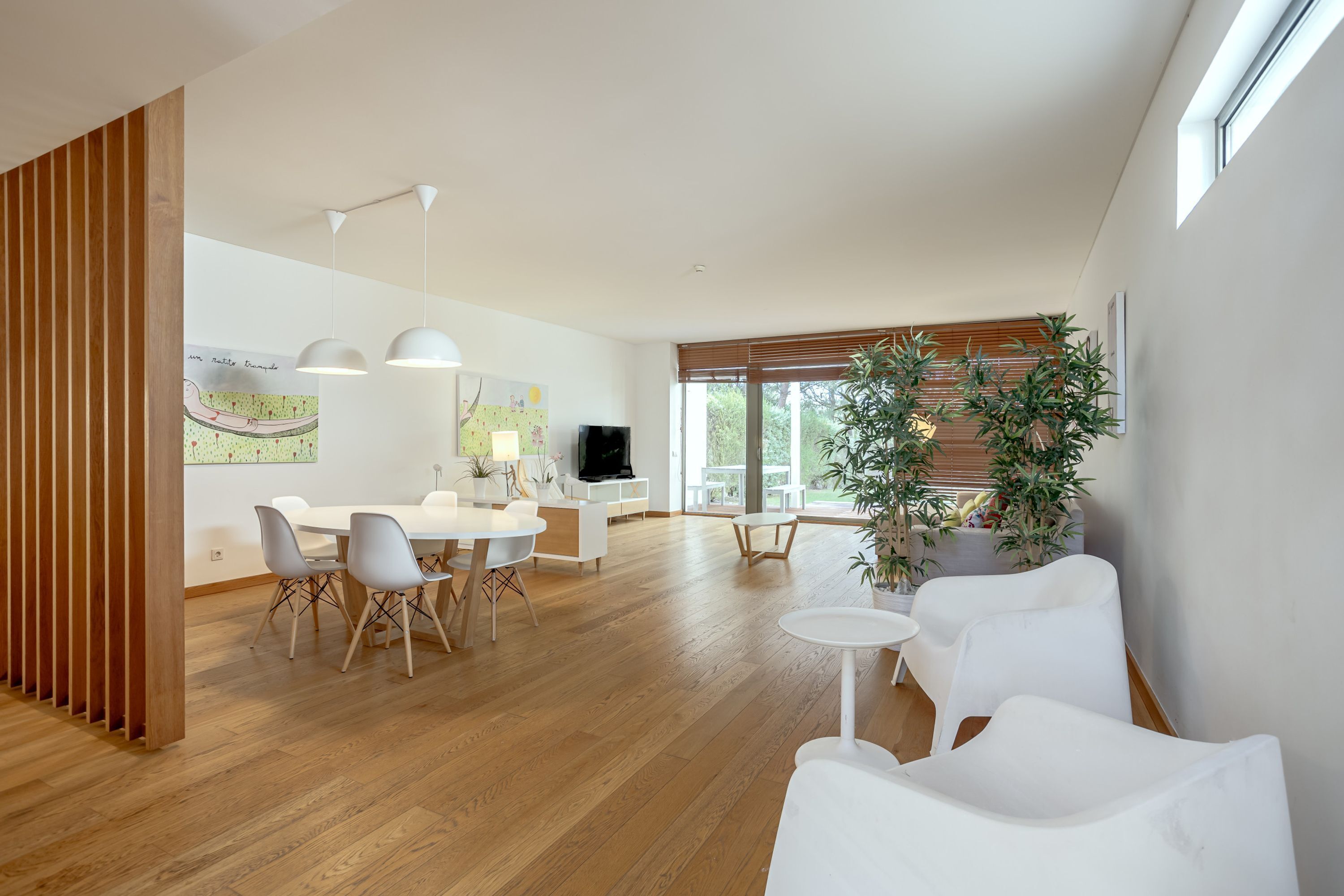 A modern living space with a dining area, white furniture, and a large window providing natural light.