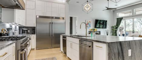 A modern kitchen with stainless steel appliances, white cabinetry, and a marble island.